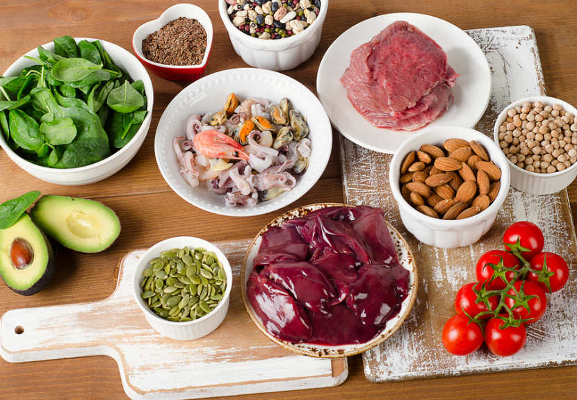 Table set with a variety of foods containing high levels of zinc, including sea food, almonds, sun flower seeds, avocadoes, and spinach.